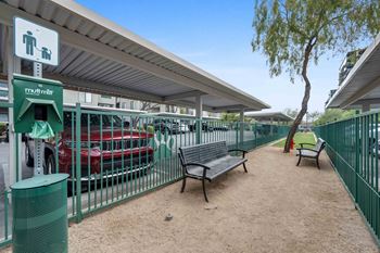 a bench and trash can in front of a green fence